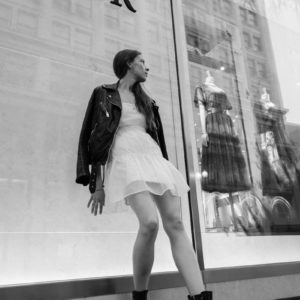 woman in white dress and black leather jacket standing in front of glass wall